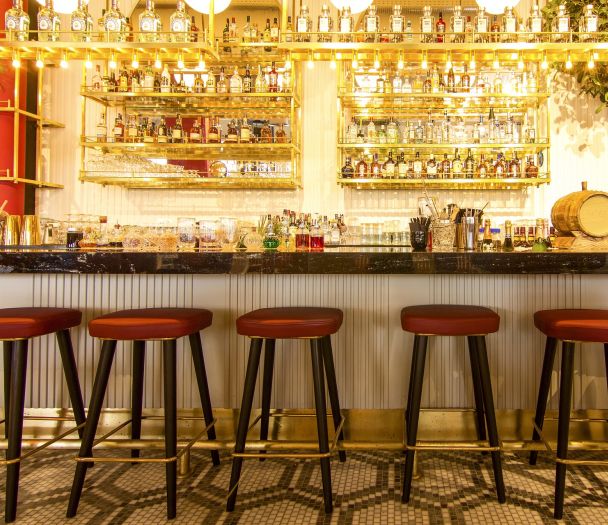 chair-3034956_1920 608x525 a bar with shelves of bottles lit up and red stools